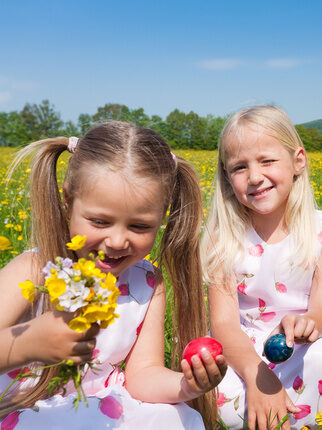Drei kleine M&auml;dchen halten Ostereier in der Hand w&auml;hrend sie auf einer Wiese sitzen